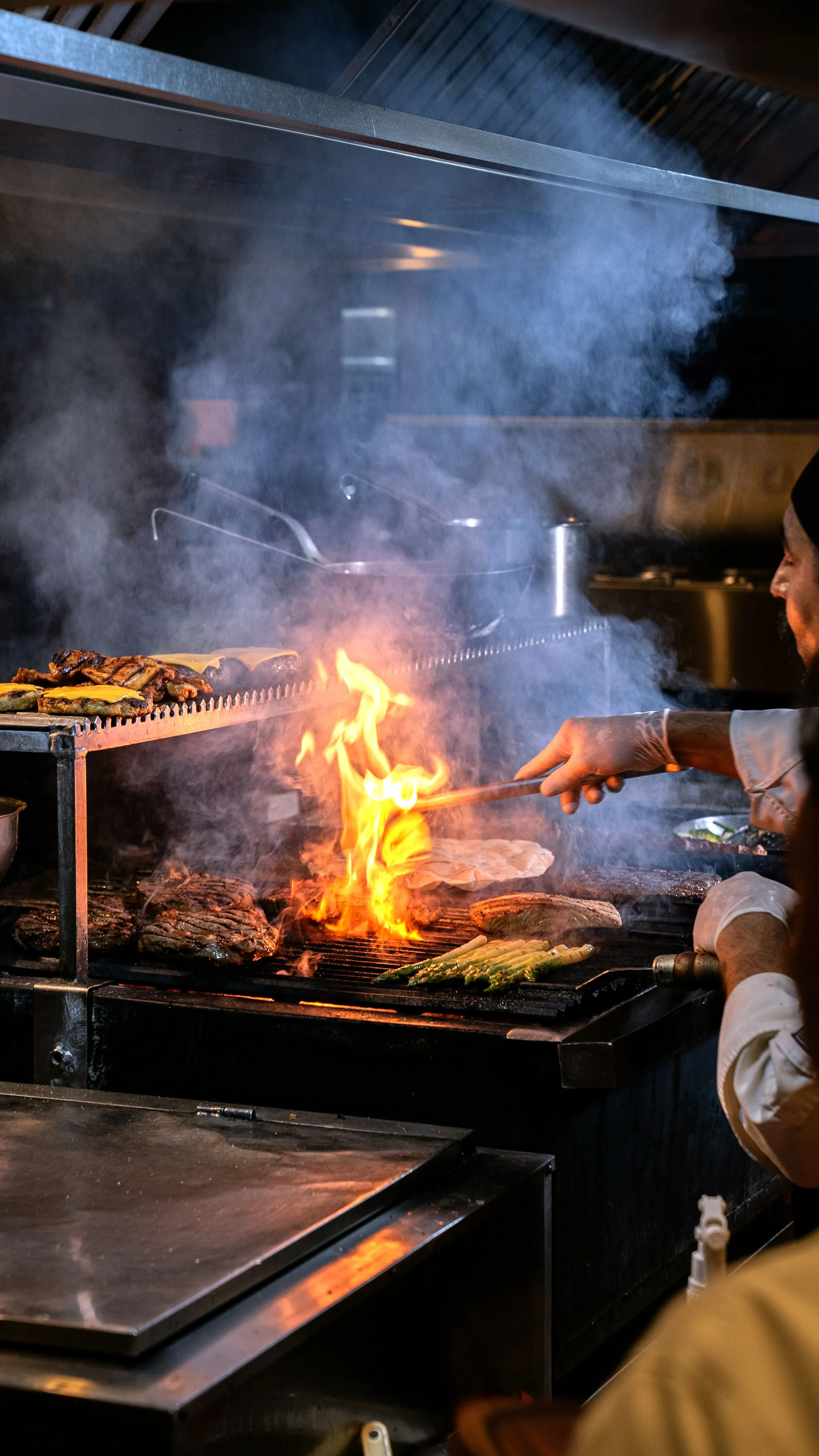 Nuestra cocina de brasa en plena faena, con las llamas subiendo entre el humo